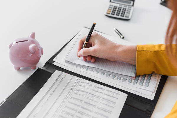 Hand writing on financial documents beside piggy bank