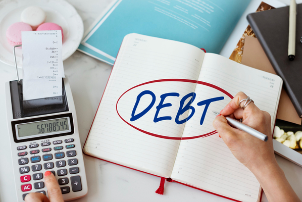 Calculator and notebook with debt written showing tax debt forgiveness program planning.